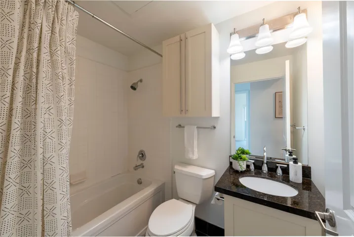 Full bathroom featuring a tub/shower combination with white tile surround, a built-in vanity with a dark speckled countertop, an undermount sink, and a mirrored medicine cabinet