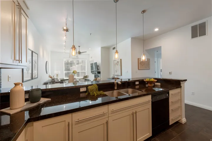 Kitchen featuring dark stone countertops, stainless steel double sink, and light-toned cabinetry with brushed nickel hardware