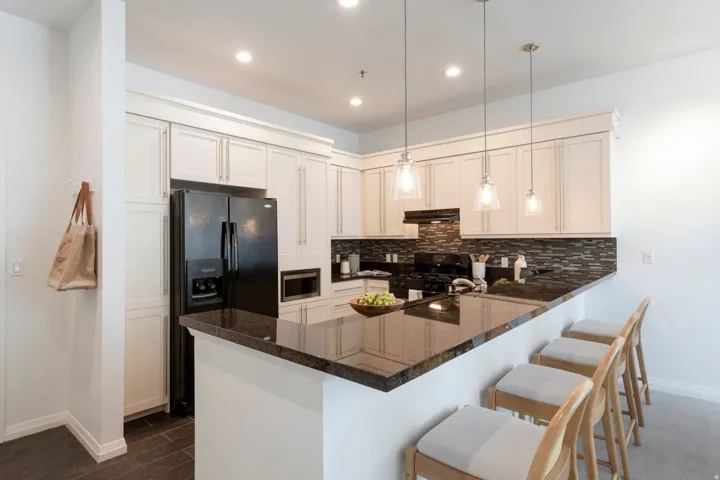 Modern kitchen featuring a breakfast bar with seating, dark countertops, white cabinetry with crown molding, and a dark tile backsplash