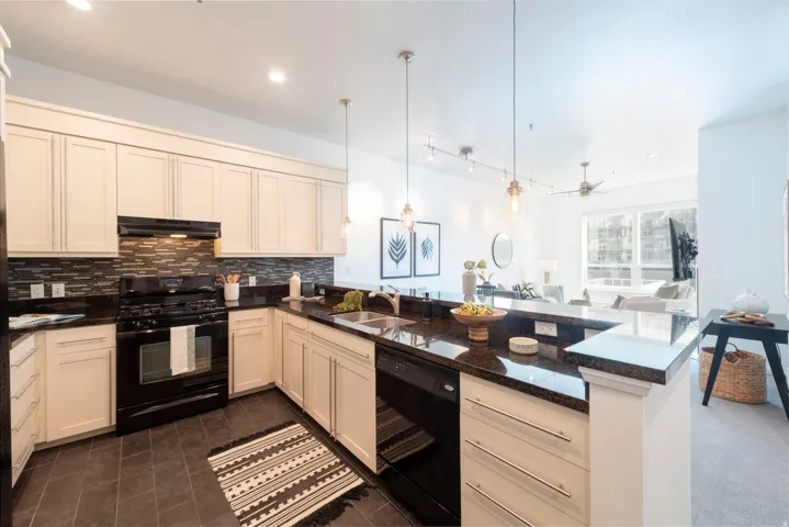 Kitchen featuring white cabinetry, dark stone countertops, a black tile backsplash, and stainless steel sink