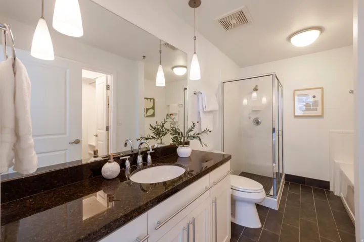 Spacious bathroom featuring a dark stone countertop, white vanity with chrome hardware, and a glass-enclosed shower