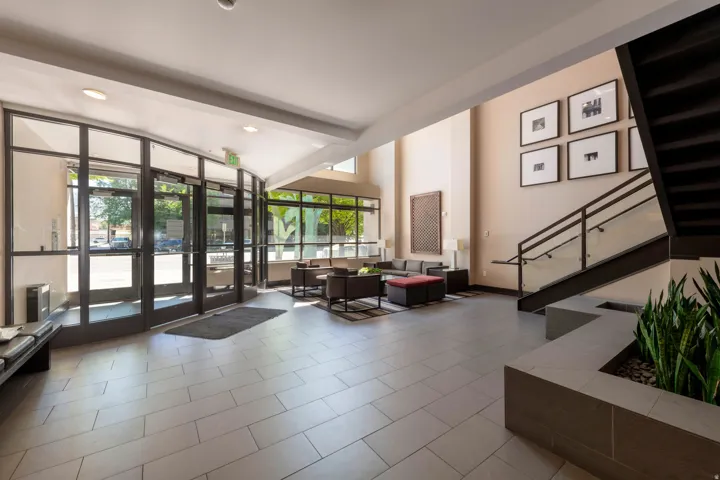 Spacious lobby with floor-to-ceiling glass entry, tiled flooring, high ceilings, an open staircase with glass railing, and a built-in planter with greenery