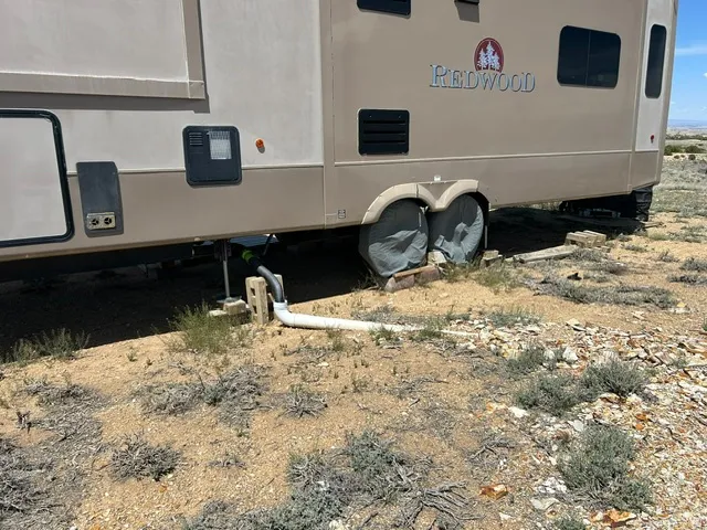 Fifth-wheel recreational vehicle with a neutral-toned exterior, featuring a "Redwood" brand emblem, tinted windows, and external utility access points
