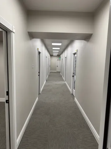 Long hallway with neutral-toned walls, recessed lighting, and carpet tile flooring