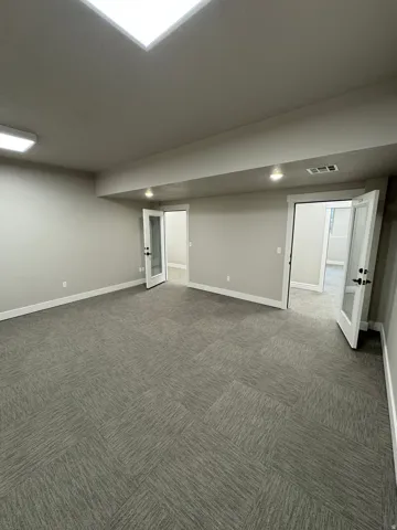 Spacious room featuring textured carpet squares, neutral wall paint, white baseboards, and multiple ceiling light fixtures