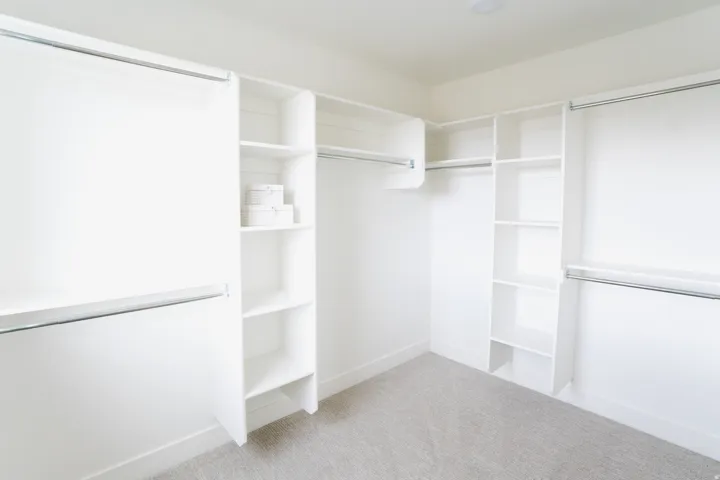 Walk-in closet featuring white built-in shelving, multiple hanging rods, recessed lighting, and light-colored carpet flooring
