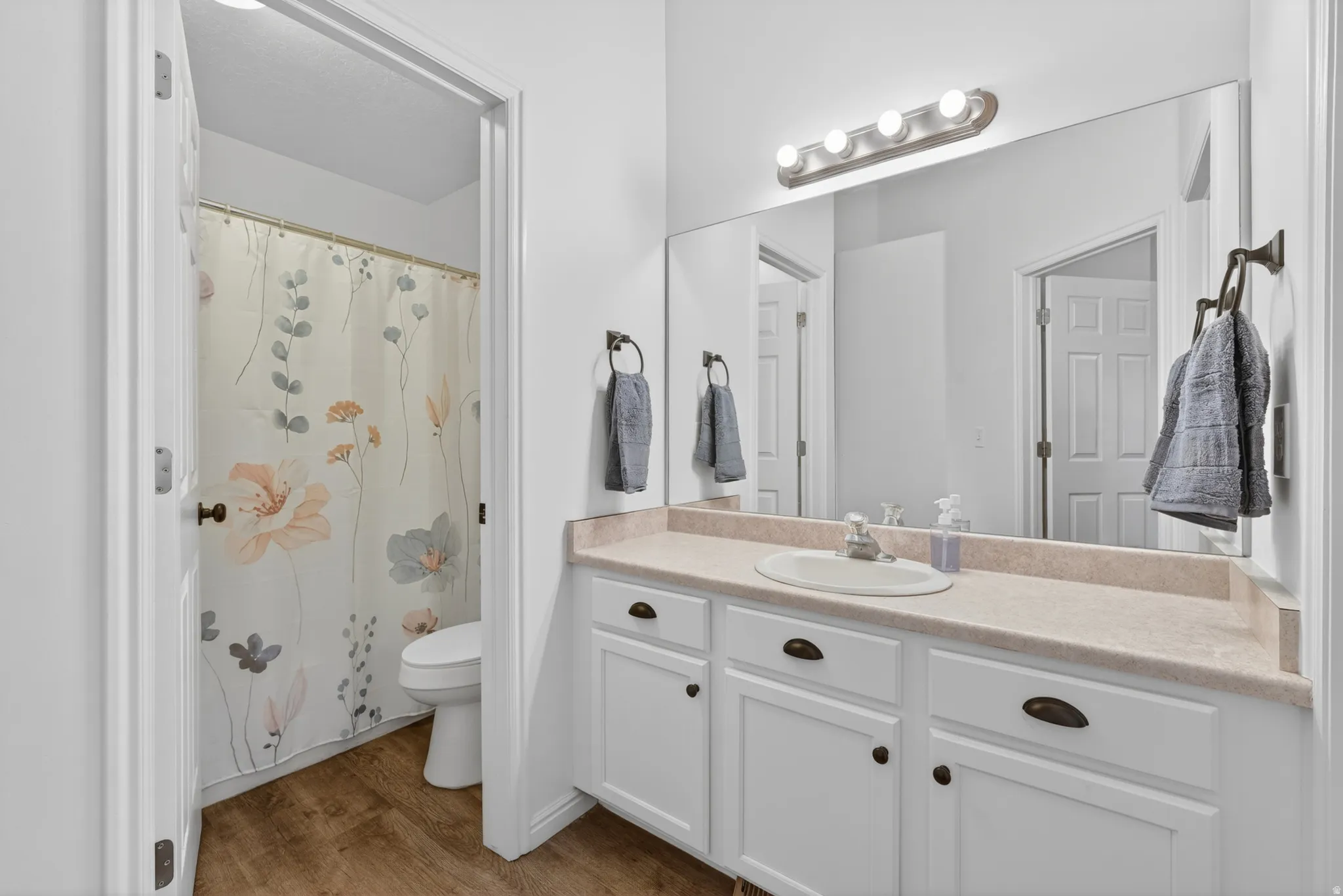 Bathroom featuring a vanity with white cabinetry, a single basin sink, a light-toned countertop, and a large wall-mounted mirror with overhead lighting