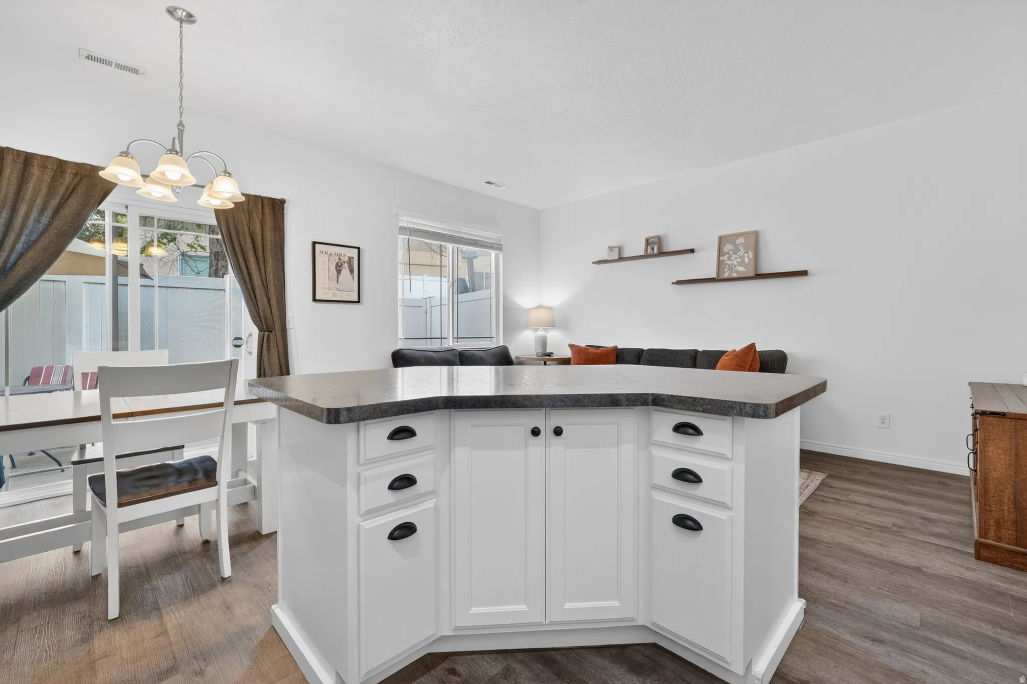 Kitchen island with white cabinetry and dark countertop, complemented by wood-finish flooring