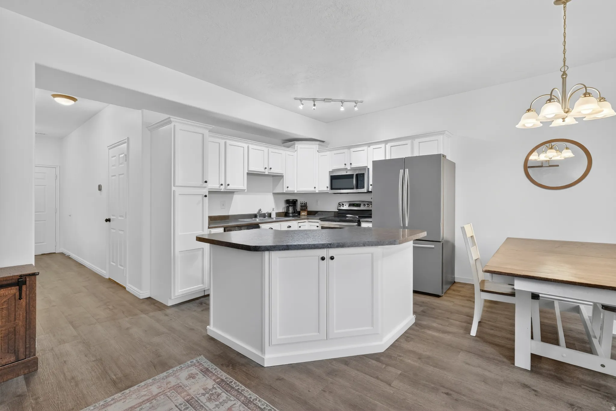 Kitchen featuring white shaker cabinetry, stainless steel appliances, a center island with countertop seating, and wood-finish flooring