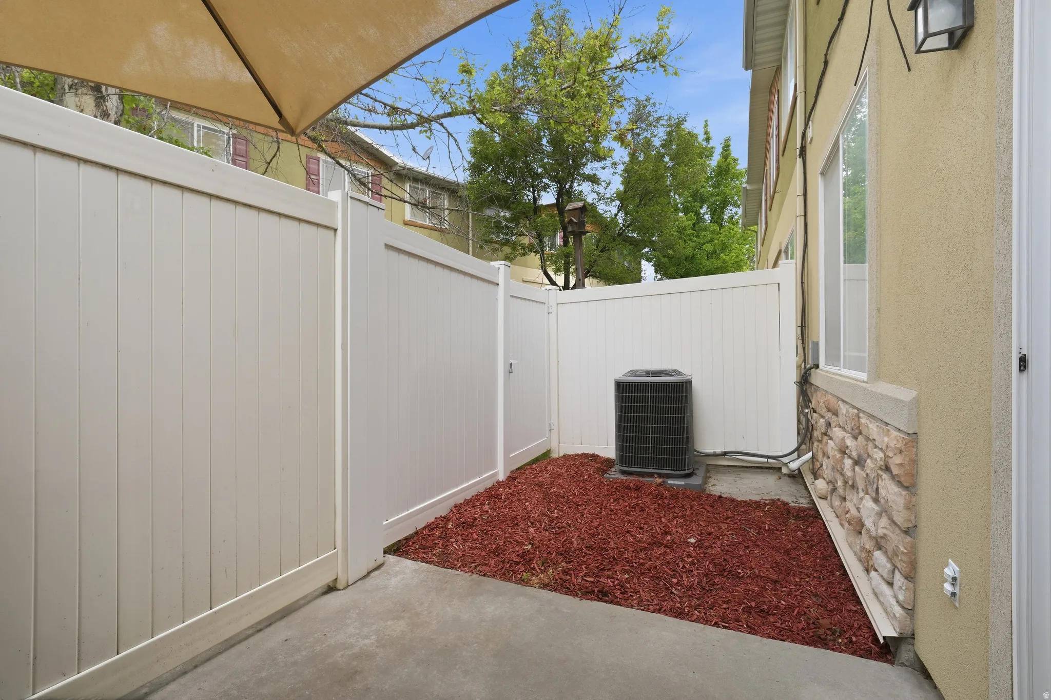 Private outdoor patio area featuring concrete paving, a neutral-toned privacy fence, a stucco exterior, and a stone accent wall