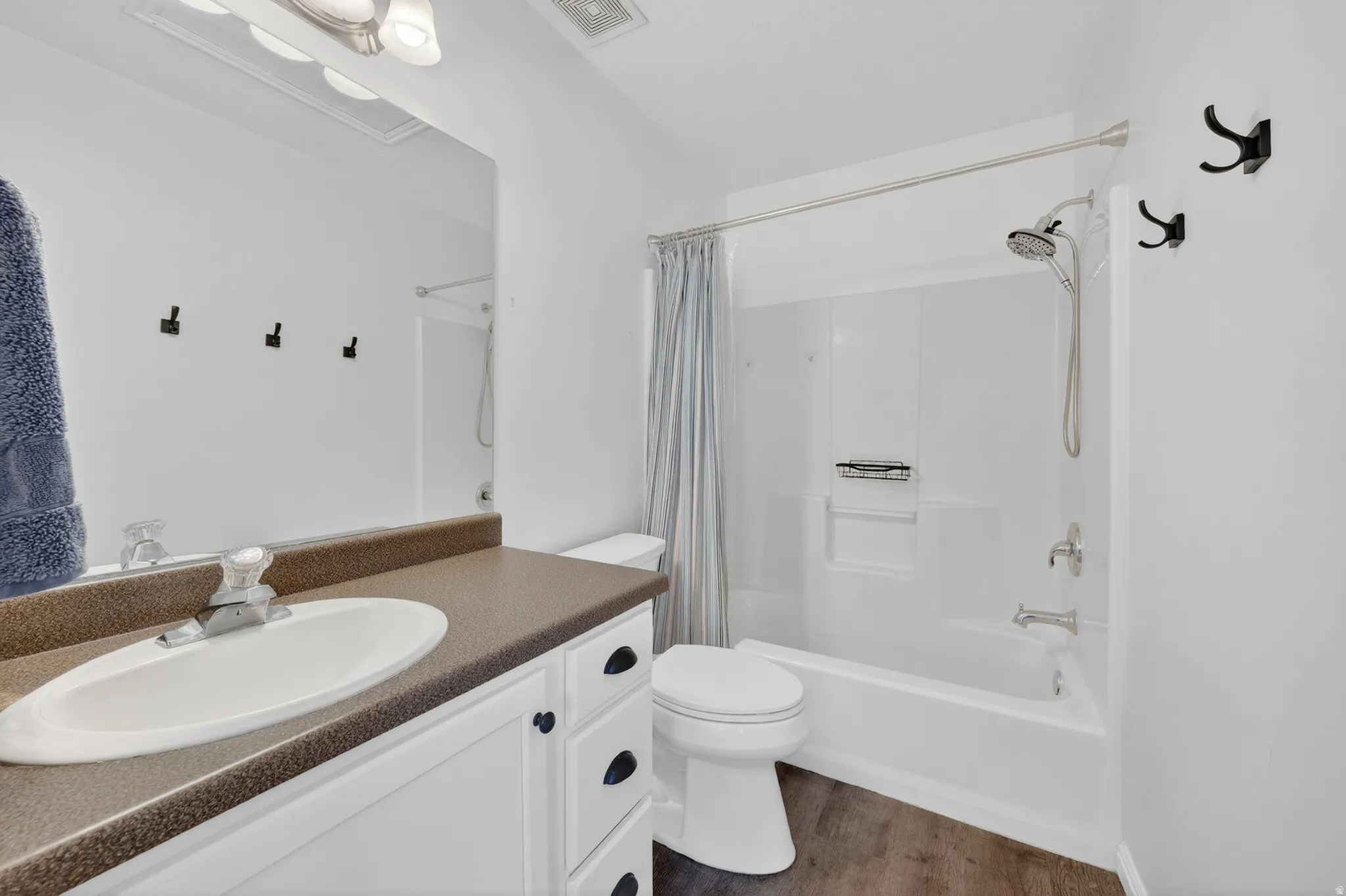 Bathroom featuring a single vanity with an oval sink and dark countertop, white cabinetry with black hardware, a toilet, and a combined tub and shower unit with a showerhead and separate handheld sprayer