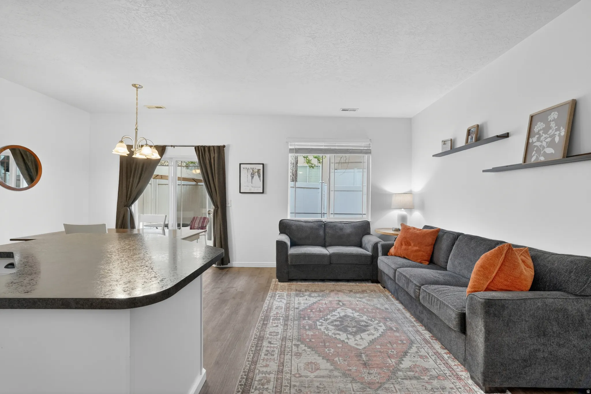 Open-concept living area featuring wood-finish flooring, white walls, and a large kitchen island with a dark countertop