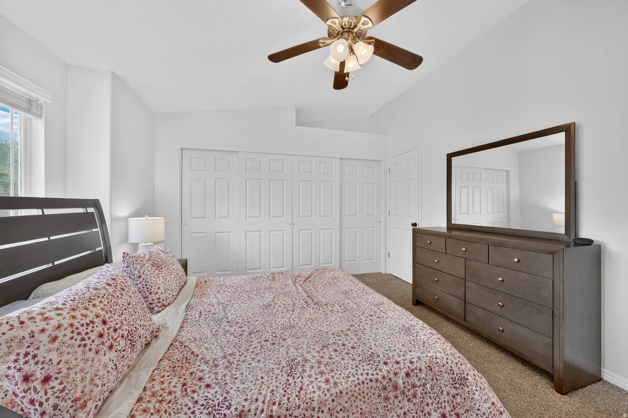 Carpeted bedroom featuring vaulted ceilings, a ceiling fan with integrated lighting, and white bi-fold closet doors