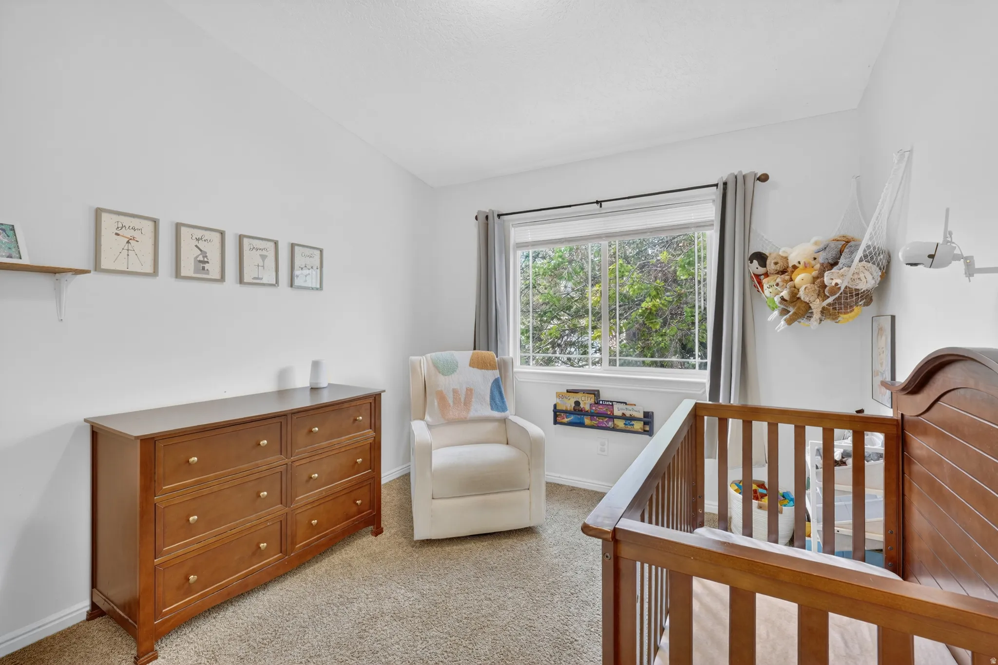 Carpeted room with a double-pane window, white walls, and a light brown wood-finish dresser with six drawers