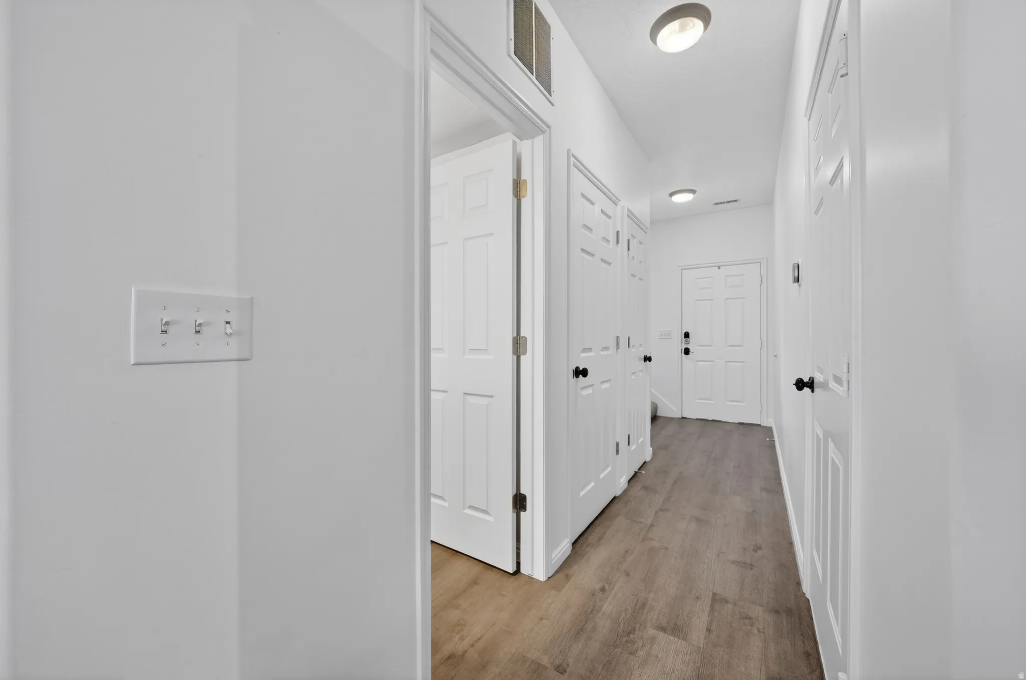 Hallway featuring wood-finish flooring, white panel doors with black hardware, and recessed lighting fixtures