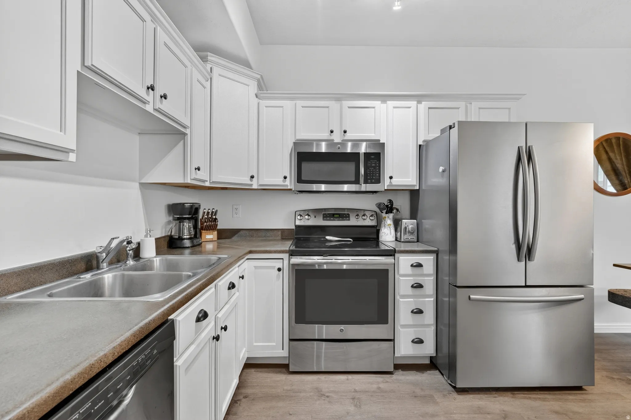 Kitchen featuring white cabinetry with dark hardware, stainless steel appliances, a double basin sink, and a durable countertop