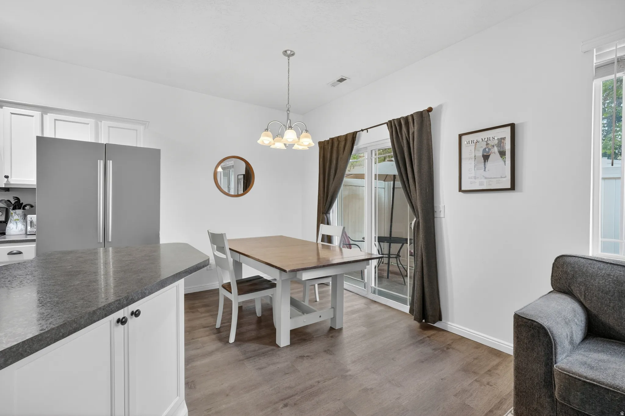 Open-concept dining area featuring wood-finish flooring, a contemporary chandelier, and a sliding glass door providing access to an exterior patio