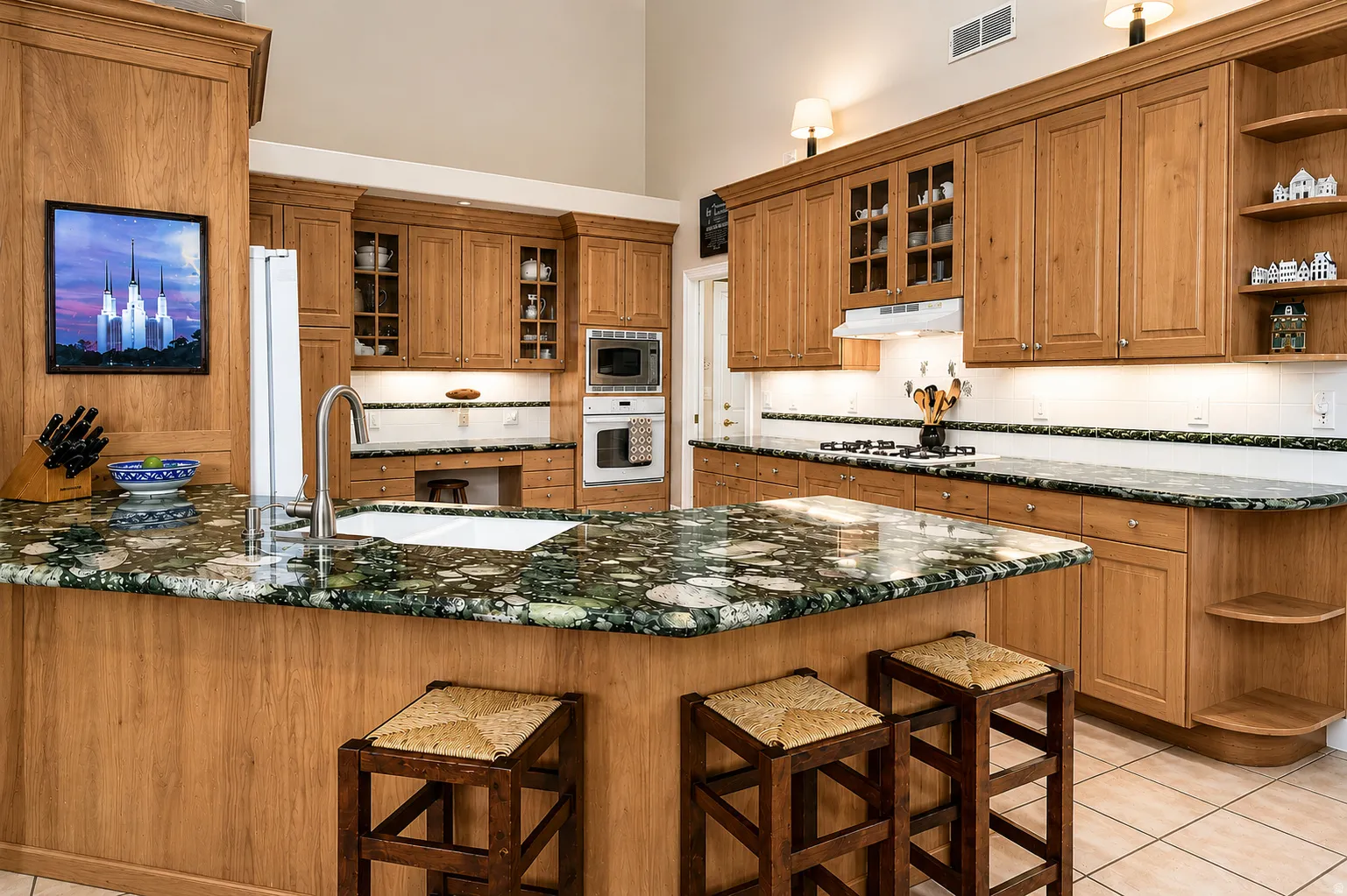 Kitchen featuring a central island with a built-in sink and granite-finish countertop, light wood cabinetry, white tile backsplash, and stainless steel appliances including a wall oven and microwave