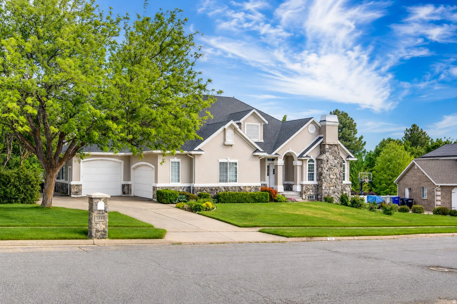 Stucco exterior with stone accents, featuring a multi-car garage, manicured lawn, and mature landscaping