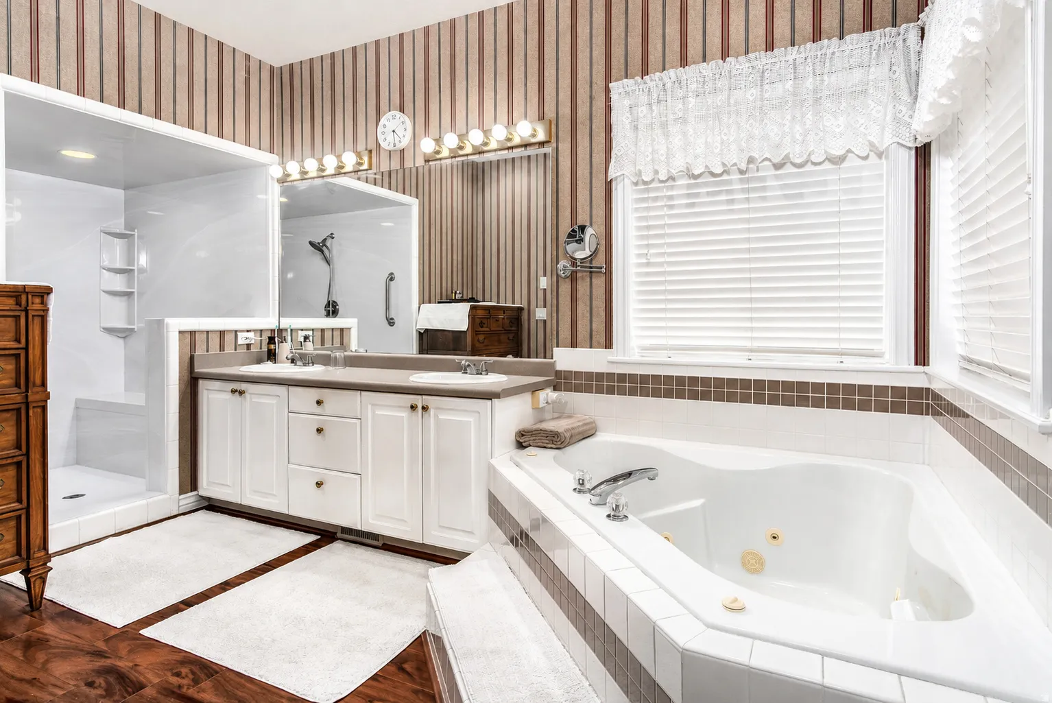 Spacious bathroom featuring a built-in jetted tub, a separate walk-in shower, a double vanity with two sinks, and wood-finish flooring