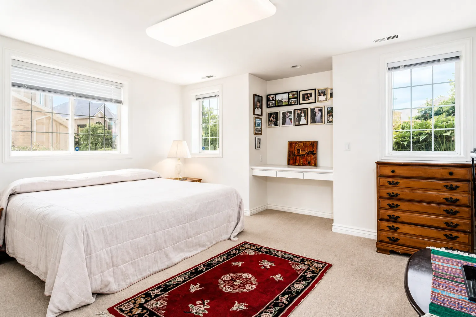 Carpeted room featuring multiple windows with grid patterns, a built-in desk with a white countertop, and a rectangular flush-mount ceiling light