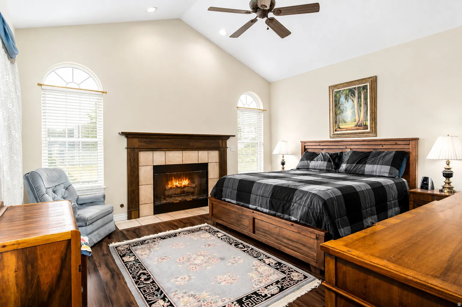 Room featuring a vaulted ceiling with a ceiling fan, a fireplace with a wood mantle and tile surround, and wood-finish flooring