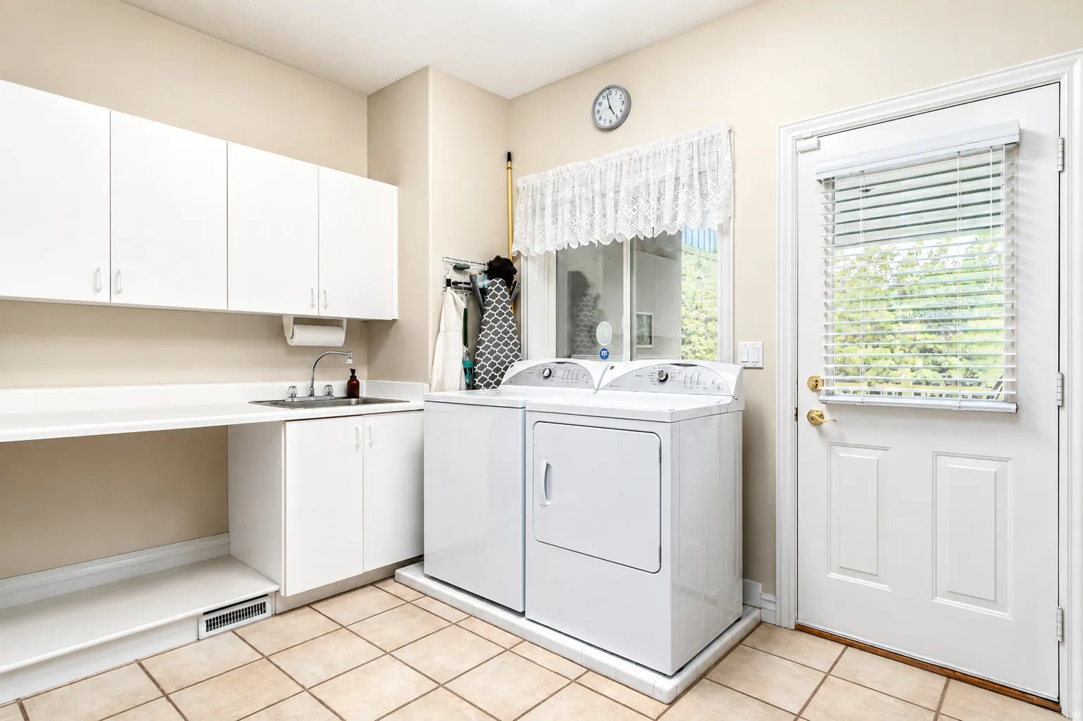 Dedicated laundry space featuring a utility sink, white cabinetry, a window, and tile flooring
