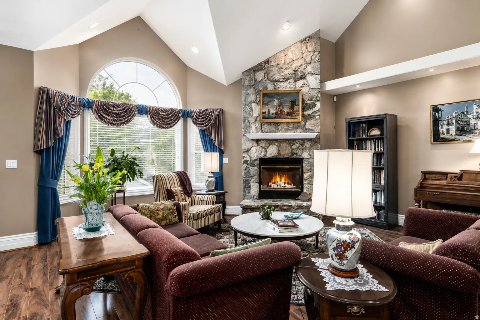 Living area featuring a stone-clad fireplace, high vaulted ceilings, an arched top window, wood-finish flooring, and recessed lighting