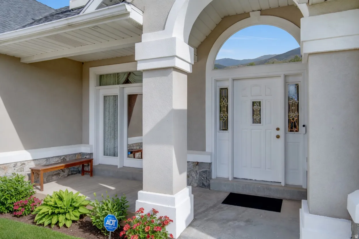 Arched entryway featuring a paneled white door with decorative glass inserts and sidelights, complemented by a stone foundation and stucco exterior