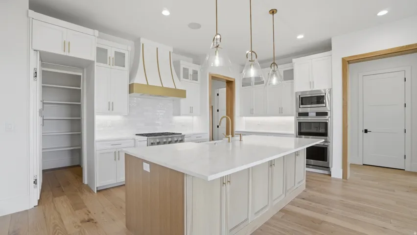 Gourmet kitchen featuring a large central island with seating, white cabinetry, integrated stainless steel appliances, a walk-in pantry, and wood-finish flooring