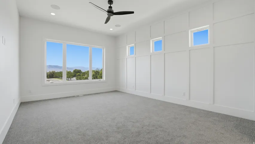Spacious room featuring a multi-pane window with mountain scenery, board and batten accent wall with high transom windows, recessed lighting, and a ceiling fan