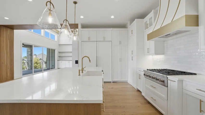 Contemporary kitchen featuring a large island with a light-toned countertop, a professional-grade range, white cabinetry, a decorative range hood, and light wood-finish flooring