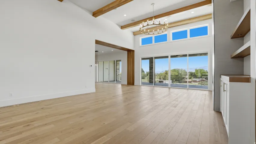Vaulted ceiling with exposed wood beams, wood-finish flooring, built-in shelving, large sliding glass doors, and a decorative chandelier