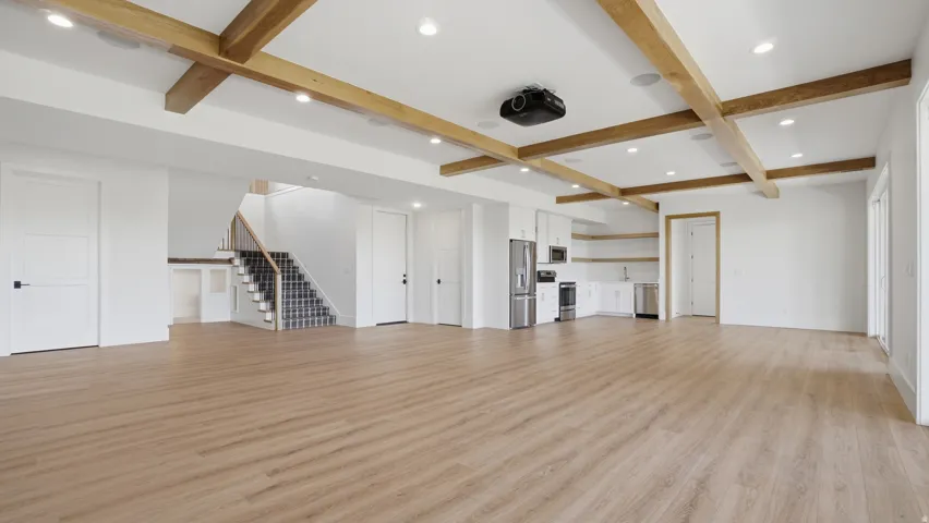 Expansive room with wood-finish flooring and a coffered ceiling featuring wood beams and recessed lighting