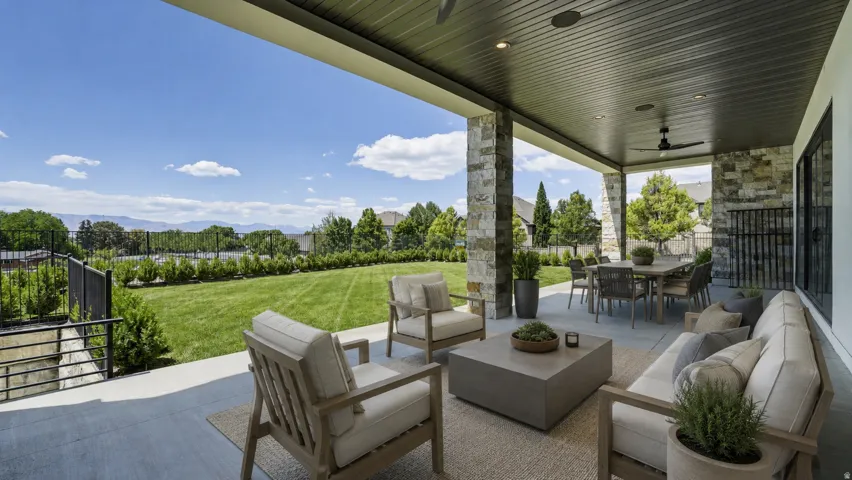 Expansive covered patio featuring stone-clad pillars, a dark paneled ceiling with recessed lighting and a ceiling fan, and a large dining area