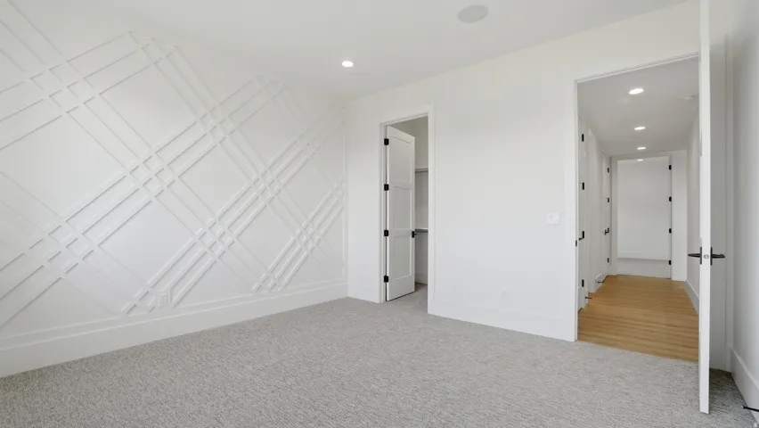 Room featuring a decorative accent wall with geometric paneling, light-colored carpeting, recessed lighting, and a doorway to a closet with bi-fold doors