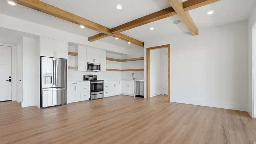 Open-concept living area featuring a full kitchen with stainless steel appliances, white cabinetry, and wood-finish flooring