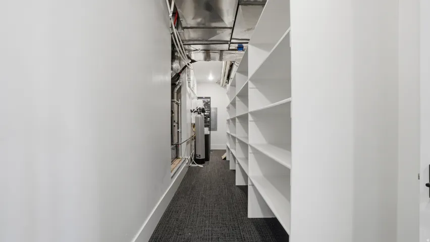 Hallway featuring extensive built-in shelving, white walls, and dark patterned carpeting