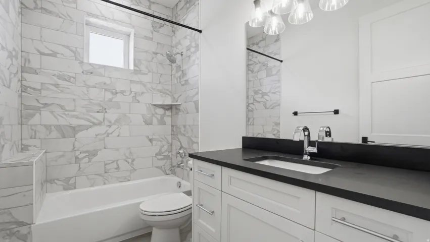 Bathroom featuring a built-in tub with a subway tile surround, a single vanity with a dark countertop, and a contemporary light fixture