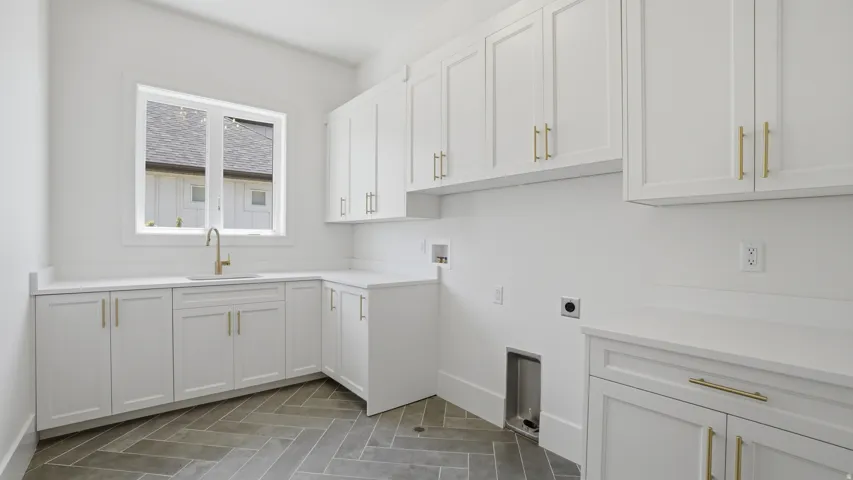 Laundry room featuring white shaker-style cabinetry with gold-tone hardware, white countertops, an undermount sink with a gooseneck faucet, and herringbone pattern floor tiles