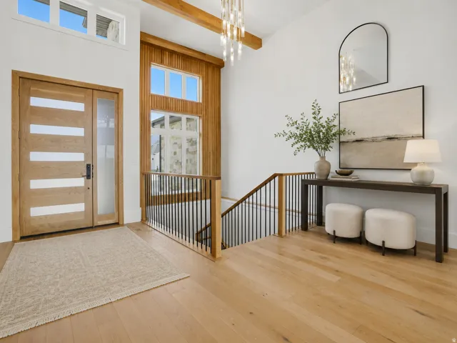 Two-story entry featuring light wood-finish flooring, a modern chandelier, and a wood-paneled accent wall