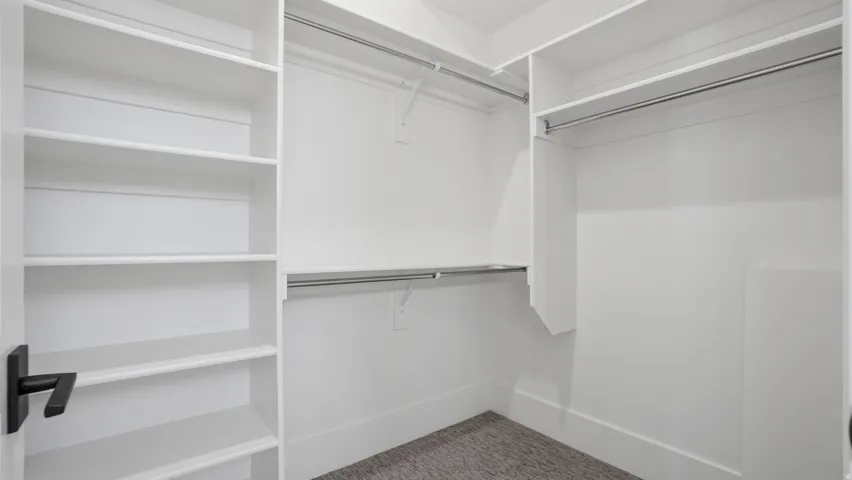 Walk-in closet featuring built-in shelving, multiple hanging rods, white trim, and carpet flooring