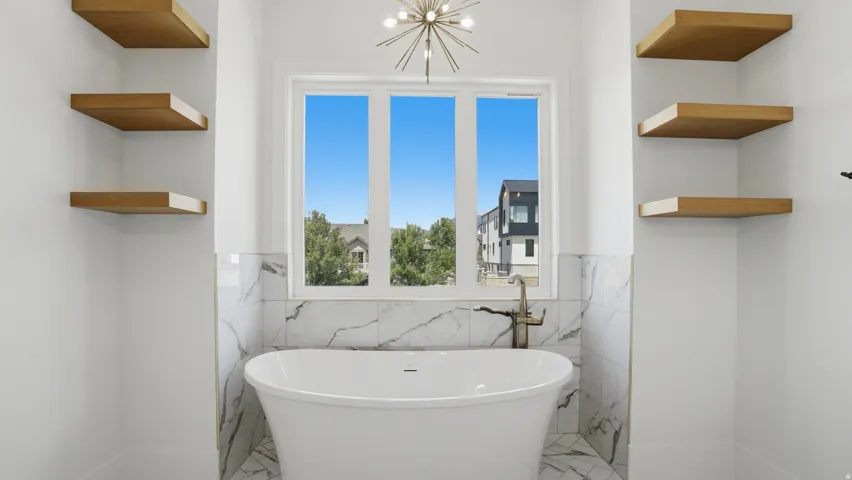 Freestanding soaking tub with floor-mounted faucet, surrounded by marble-style tile wainscoting