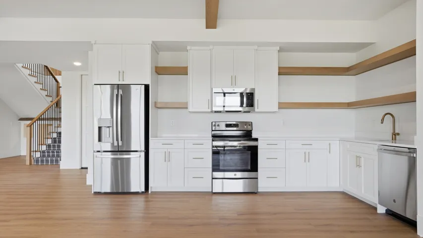 Modern kitchen featuring white shaker cabinetry, stainless steel appliances, open shelving, and wood-finish flooring