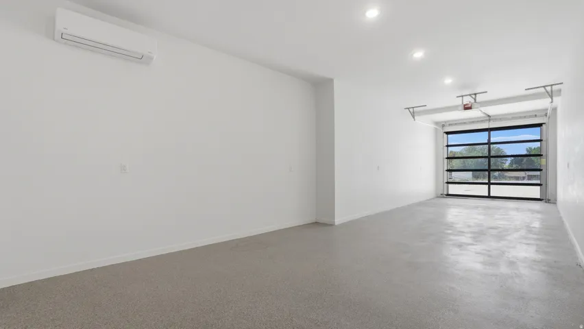 Spacious interior featuring a full-view garage door, recessed lighting, polished concrete flooring, and a wall-mounted mini-split HVAC unit