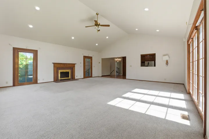 Spacious living area featuring a vaulted ceiling with recessed lighting, an elegant fireplace with a wood mantle and brass insert, and a ceiling fan