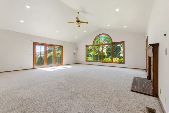 Spacious living area featuring a vaulted ceiling with recessed lighting, an expansive arched window, and a brick-hearth fireplace with a wood mantel