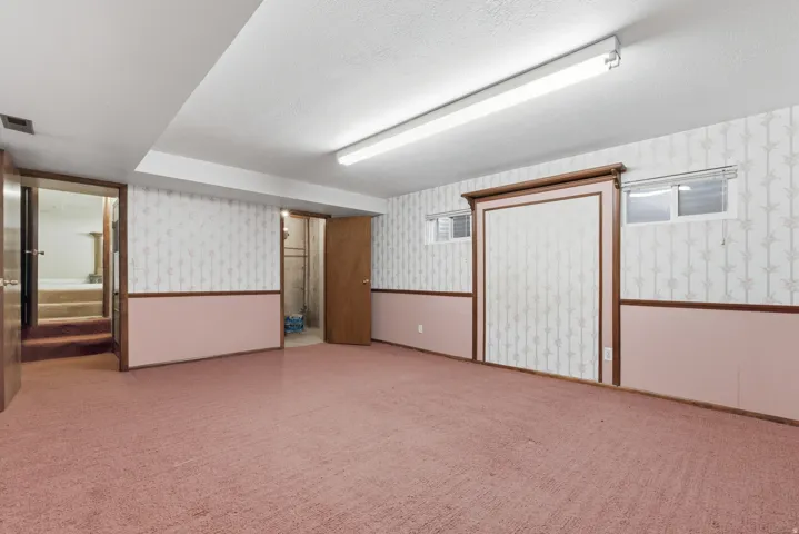 Spacious lower-level room featuring pink carpeting, wallpapered walls with a chair rail, and exposed ceiling ductwork