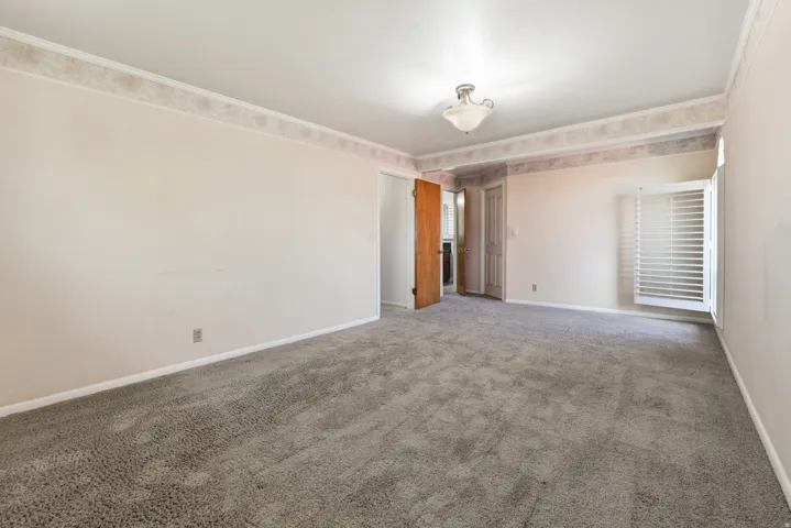 Carpeted room featuring a ceiling-mounted light fixture, light-colored walls, patterned wallpaper border, and white louvered window shutters
