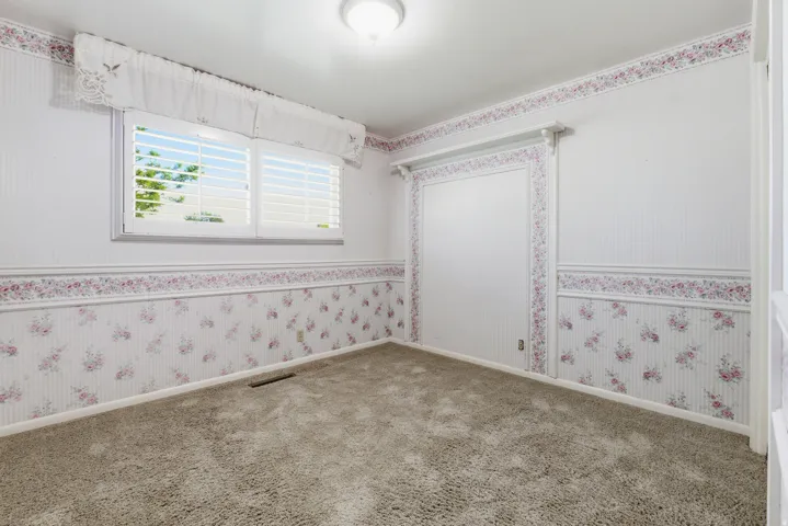Carpeted interior space featuring a window with white shutters, crown molding, a built-in wall niche, and a flush-mount ceiling light fixture
